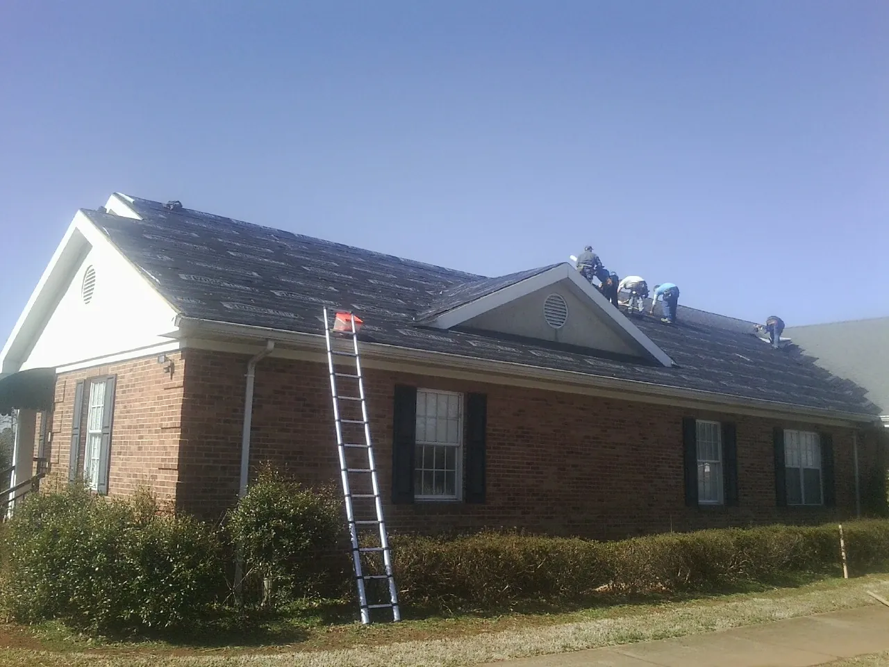 Crew tearing shingles off a brick ranch roof with a ladder set — Emergency Roof Repair work by our crew in Valley Falls