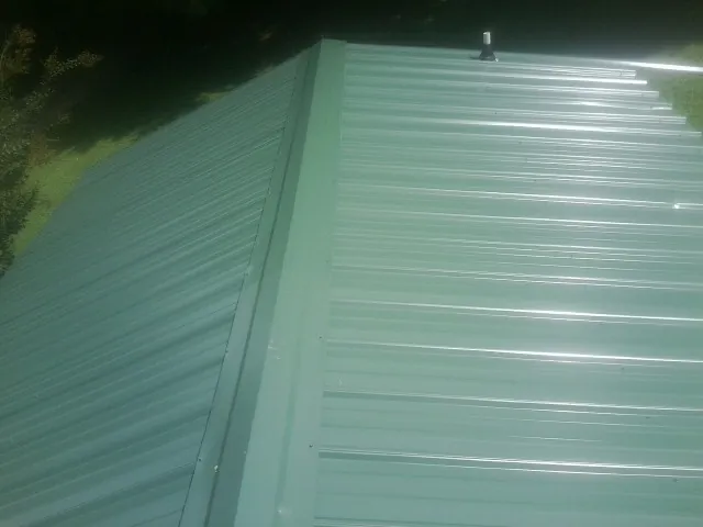 New green metal panels meeting at the ridge of a roof — Flat Roof Repair work by our crew in Valley Falls