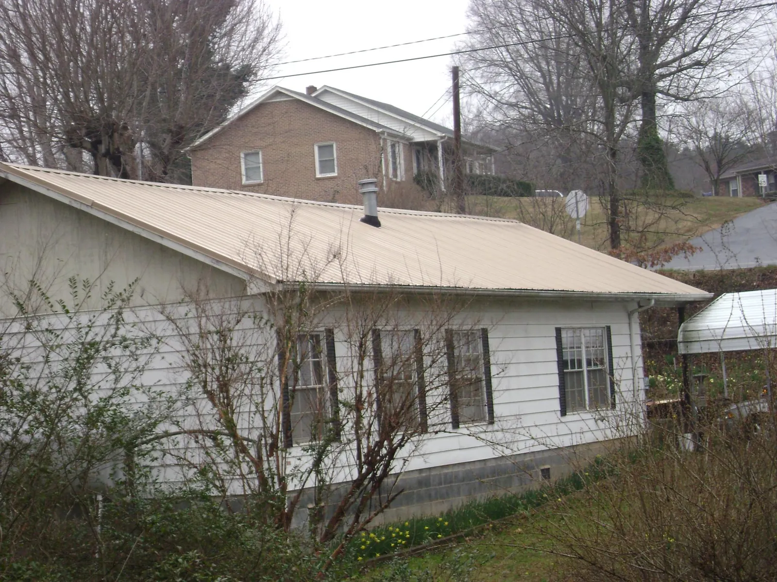Tan metal roof on a white sided house set into a hillside — Commercial Roofing by Roofing Brothers in Valley Falls